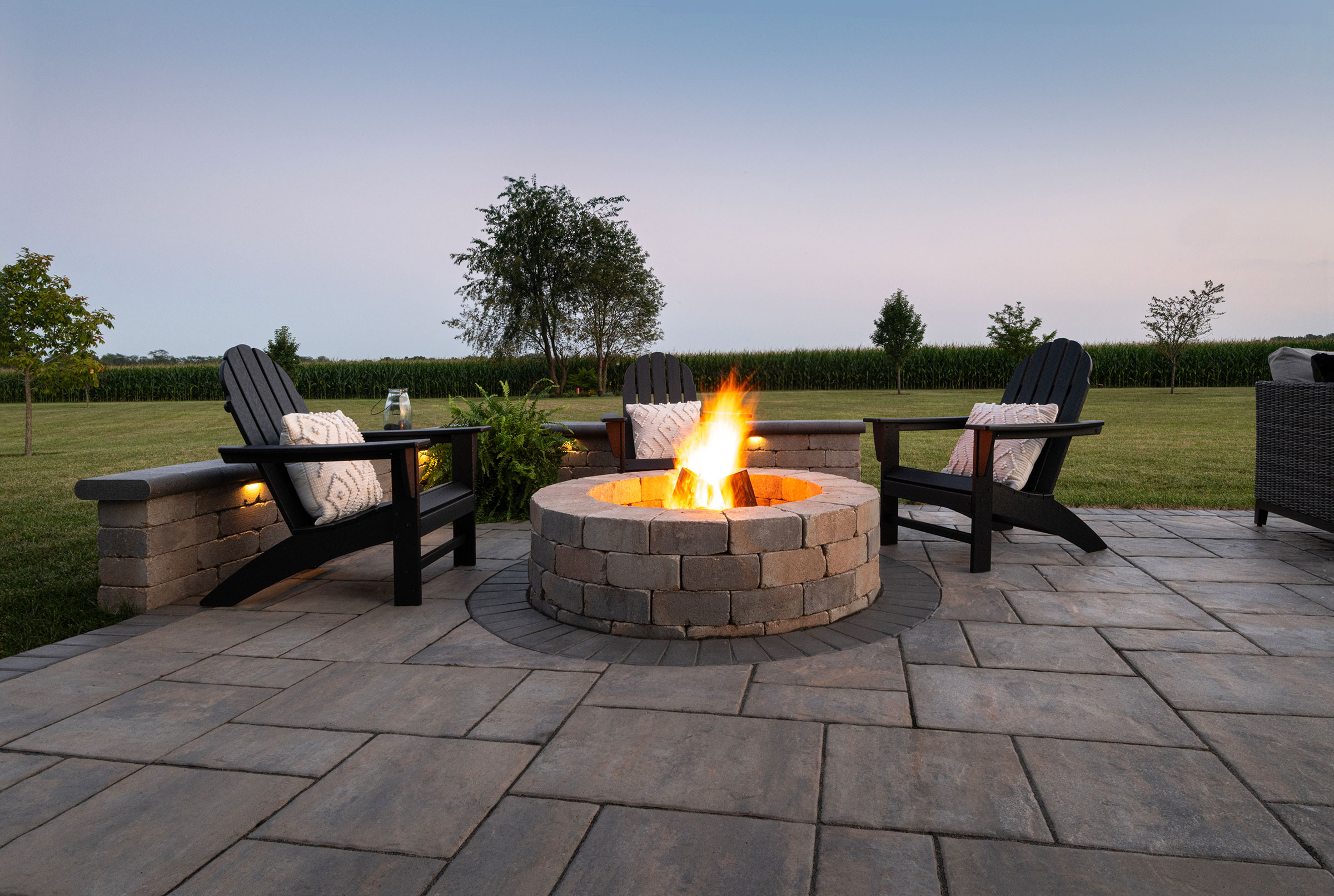 Round paver fire pit at dusk with adirondack chairs